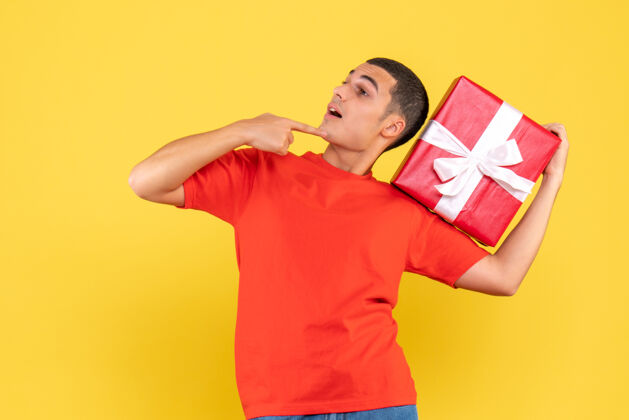 庆祝黄色墙上手持圣诞礼物的年轻人的正视图盒子礼物举行