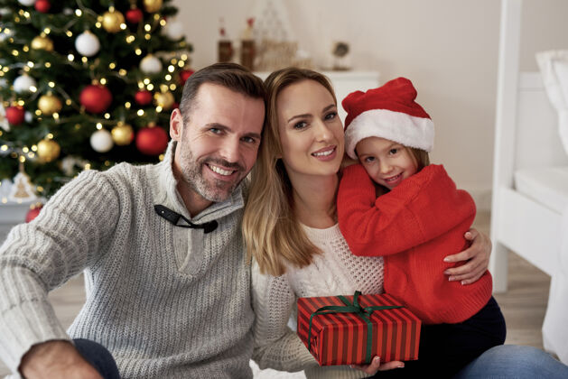 女孩带着圣诞礼物的微笑家庭的画像关闭前面腰部向上