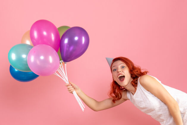 节日粉红色墙上手持彩色气球的年轻女子的正视图庆祝女性年轻女性