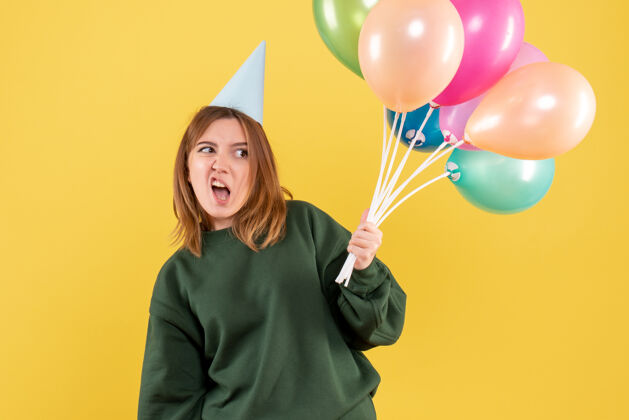 女性正面图：带着彩色气球的年轻女性生日颜色吹