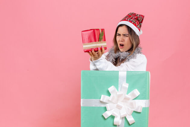 圣诞节一个年轻的女人拿着另一个礼物在粉红色的墙内的正面视图人庆祝快乐