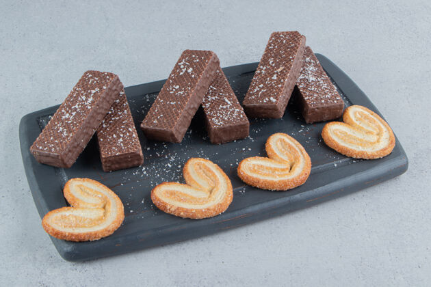 片状巧克力华夫饼和薄饼放在大理石背景的黑木板上糕点曲奇巧克力