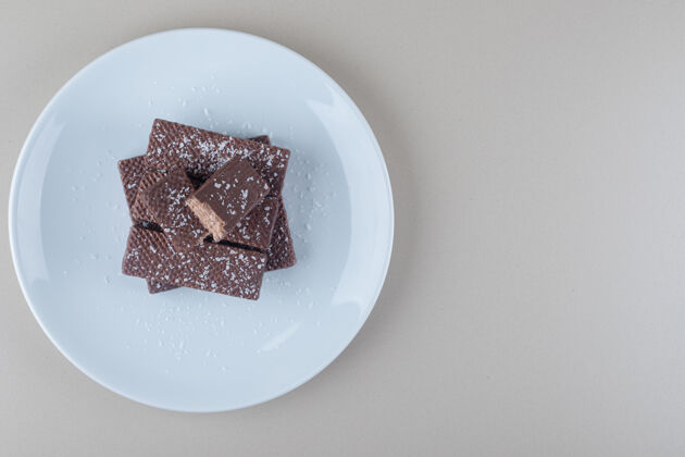 美味巧克力涂层的晶圆堆在大理石背景上的白色盘子上小吃巧克力甜点