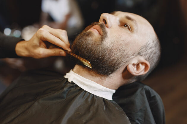 年轻人有胡子的男人有客户的理发师有梳子和剪刀的男人小胡子理发师修饰