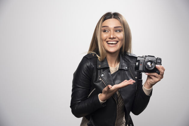摄影师一位身穿黑色皮夹克的年轻女士 以积极微笑的态度用相机拍照摄影快乐相机