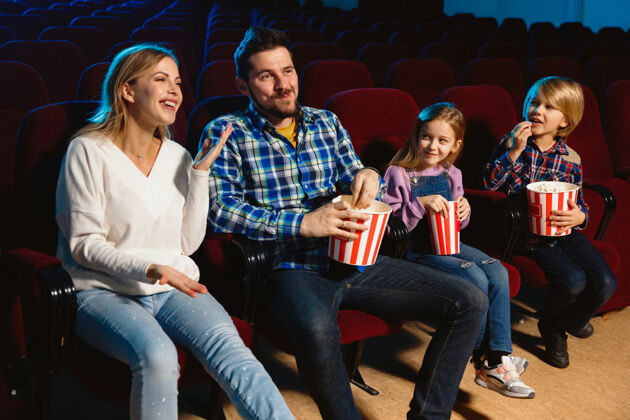 乐趣年轻的白种人家庭在电影院 房子或电影院看电影看起来富有表现力 惊讶和情绪化独自坐着玩关系 爱情 家庭 童年 周末时间看电影院座位