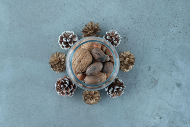 开胃的玻璃罐里的坚果堆在大理石表面的松果中间好吃的有味道的榛子