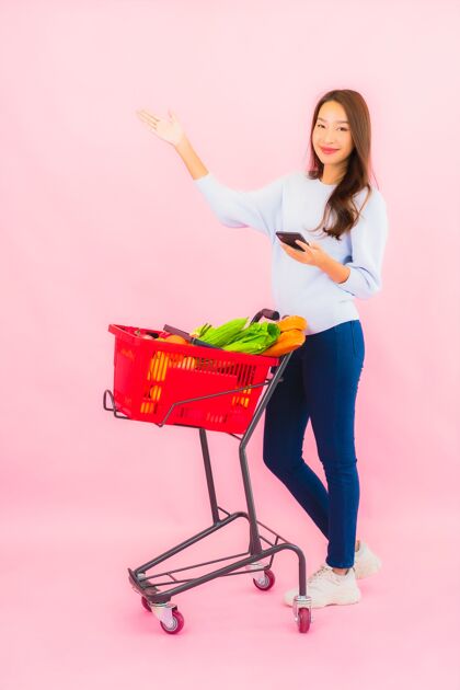 顾客一幅美丽的亚洲年轻女子的画像 粉红色的隔离墙上 篮子里放着水果蔬菜和杂货篮子购买蔬菜