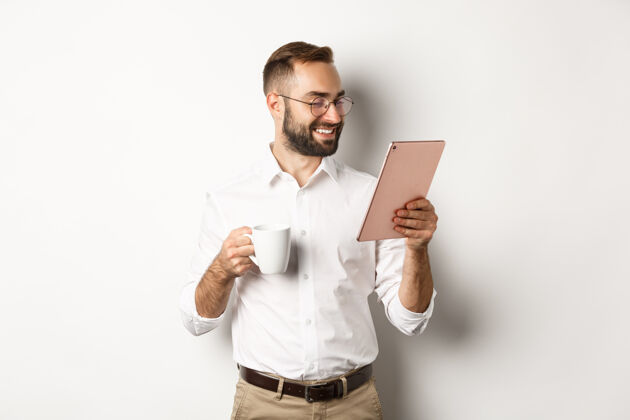 自信英俊的商人喝着咖啡 在数字平板上看书 微笑着高兴 站着科技平板电脑咖啡