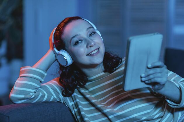 女性在家沙发上用平板电脑和耳机的女人科技人类电子产品