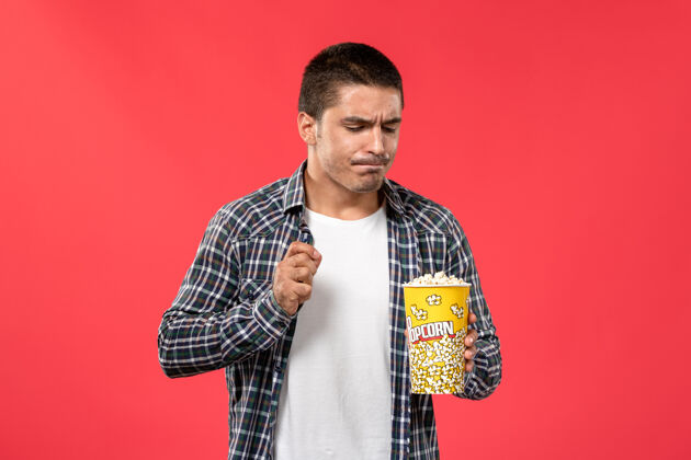 男性正面图年轻男子手持爆米花包在浅红墙电影院光包装成人