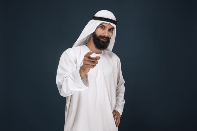 惊讶阿拉伯沙特酋长的肖像年轻的男模微笑着指着或选择茫然传统搞笑