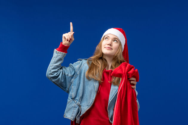欢快前视图年轻女性拿着蓝色背景上的礼物圣诞情感袋帽子漂亮节日