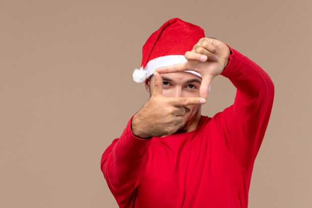成人正面图：年轻男性在圣诞假期的棕色背景上摆姿势头饰帽子脸