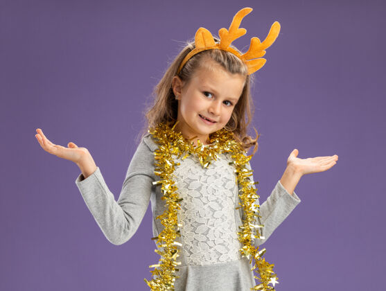 高兴可爱的小女孩戴着圣诞发箍 脖子上戴着花环 双手分开放在蓝色背景上手箍脖子