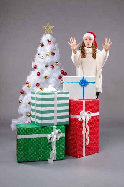 圣诞帽年轻的女性在灰色的礼物购物圣诞树庆祝