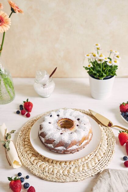 食物在白色背景的白色桌子上 一个带水果和粉末的环形蛋糕的垂直镜头甜点鲜花自制