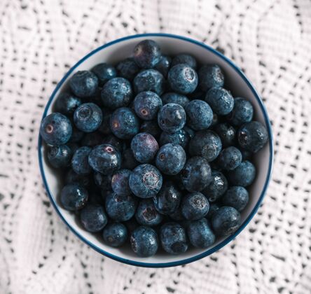 甜高角度拍摄了一个装满蓝莓的碗 放在一张漂亮的白色桌布上圆草莓浆果