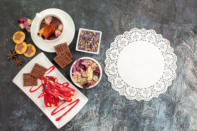 现金一块蕾丝 一盘巧克力和花草茶 干花和饼干放在灰色的地面上顶部盘子顶部视图