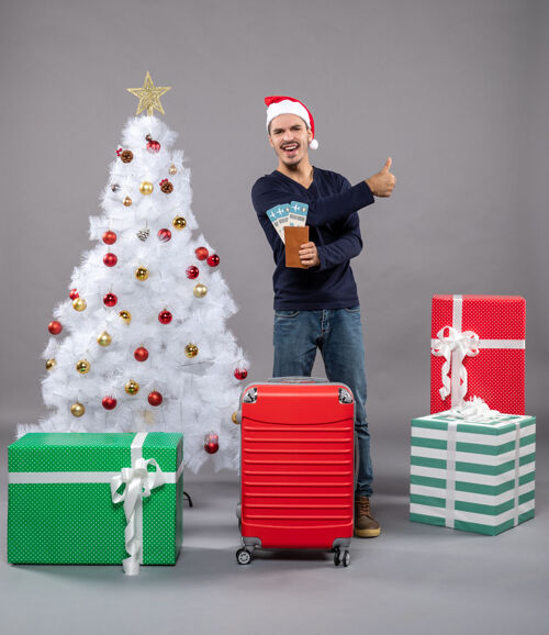 男人带着红色手提箱的笑脸男人拿着他的旅行票 向灰色竖起大拇指包手提箱圣诞老人