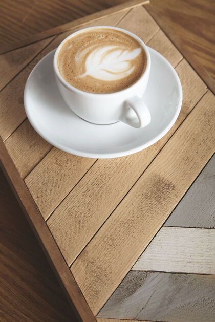浓缩咖啡茶杯侧视图 奶油卡布奇诺拿铁 顶部有乳白色泡沫 叶形 木盘上有图案咖啡厅展示桌上有自动售货机热的咖啡