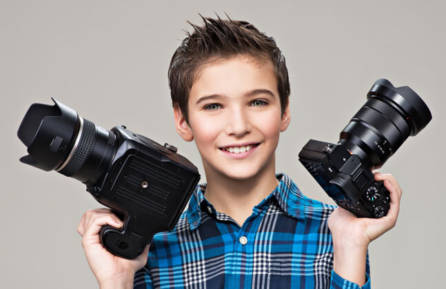 单反相机男孩拿着两个照相机微笑的白人男孩拿着单反相机在灰色背景的摄影棚里摆姿势摄影专业灰色背景