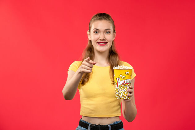 电影前视图年轻的女性在电影院拿着爆米花和微笑的红墙电影院小吃有趣的电影年轻女性女性电影