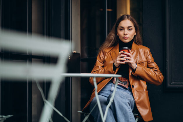 摆姿势坐在咖啡馆外面喝咖啡的年轻女孩现代咖啡饮料