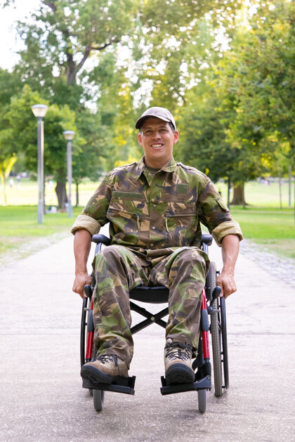旋转快乐的残疾军人在轮椅上穿着迷彩服 走在城市公园的人行道上正面视图老兵的战争或残疾概念病人轮椅移动