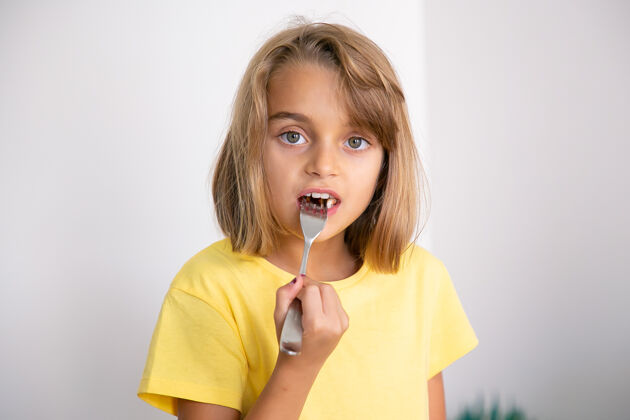 可爱可爱的金发女孩用叉子吃蛋糕的画像漂亮的白人小孩站着吃童年 庆祝和节日的概念孩子孩子小