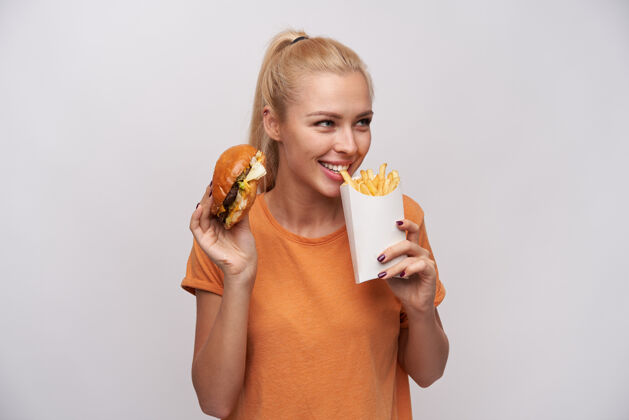 女士可爱的金发女郎 扎着马尾辫 吃着炸薯条 面带微笑 站在白色的背景上T恤天然马尾辫