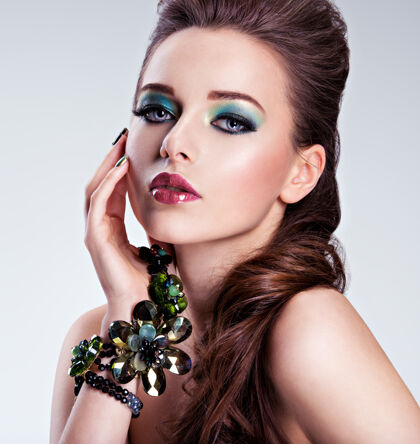 眼睛漂亮的女人脸 手上有时尚的绿色化妆品和珠宝睫毛手指珠宝