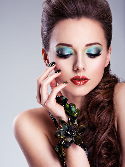 眼妆漂亮的女人脸 手上有时尚的绿色化妆品和珠宝优雅姿势明亮