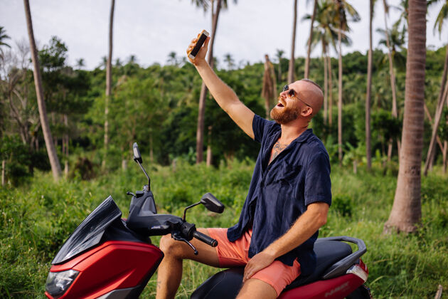 旅游在热带丛林的田野上纹着红色摩托车的壮手头盔