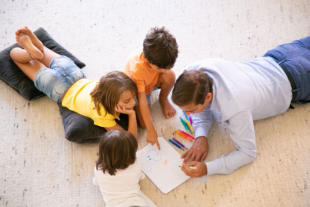 年轻专注的爸爸和孩子们躺在地毯上画画涂鸦中年爸爸用彩色钢笔画画 在家里和可爱的孩子们玩耍童年 游戏活动和父亲的概念小爸爸父亲
