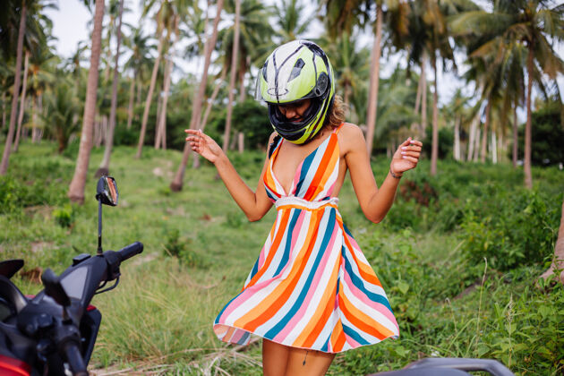 租金快乐的高加索骑摩托车的女人 穿着五颜六色的夏装 戴着摩托车头盔度假光明骑旅游