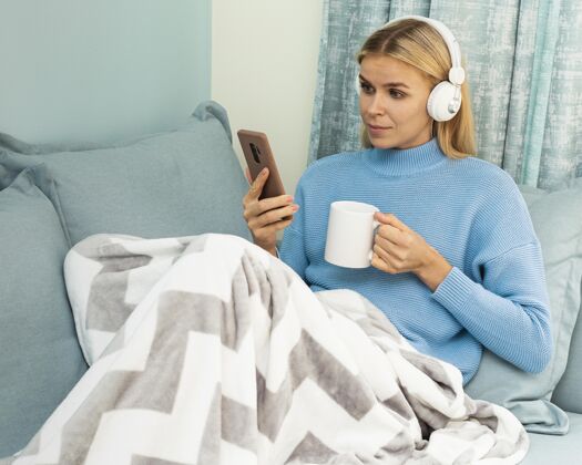 流行病大流行期间 在家喝咖啡 同时使用智能手机和耳机的妇女隐居耳机家庭