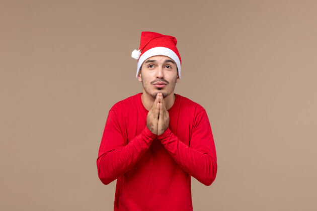 男性正面图：年轻男性在棕色背景下祈祷圣诞节表演者帽子微笑