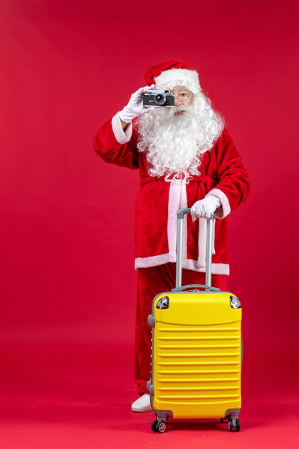 圣诞快乐前视图的圣诞老人与黄色袋拍照与相机上的红墙人旅行快乐