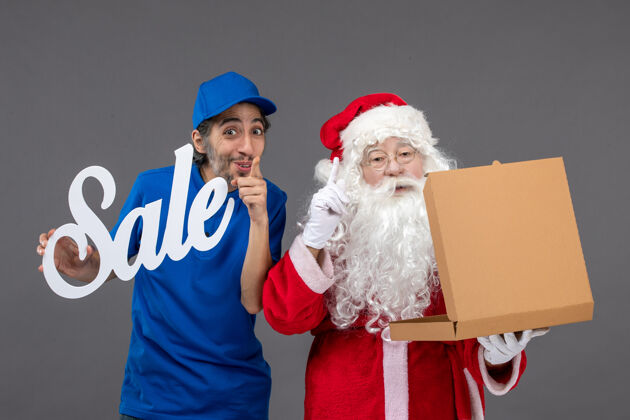 食品圣诞老人的正面图 男信使手持销售横幅 打开灰墙上的食品盒节日圣诞老人人