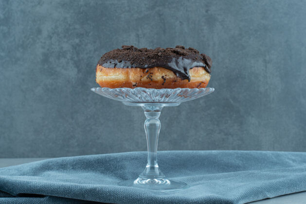巧克力甜甜圈放在玻璃基座上 放在大理石上起皱的桌布上美味美味糖