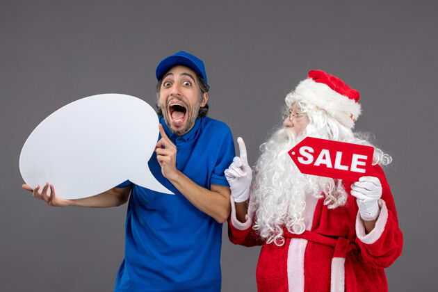 前面圣诞老人与男信使手持白色标志和灰色墙上的销售横幅的正面视图人信使圣诞快乐