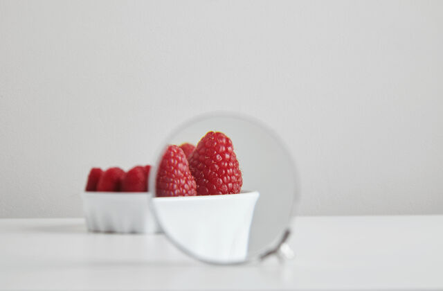 超级食品一堆成熟的覆盆子有机超级食品在陶瓷碗的概念健康饮食和营养隔离在白色的桌子上 通过放大镜放大看到细节叶子甜点有机