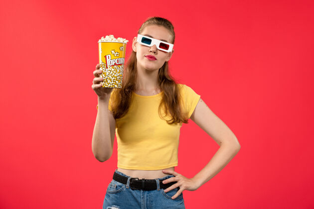 护目镜正面图年轻女子在电影院拿着爆米花包在d太阳镜上的红墙电影女孩爆米花成人观点