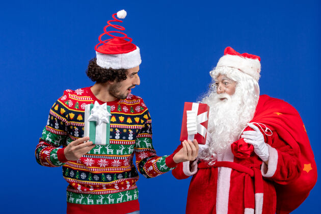 男人正面图：圣诞老人和手持礼物的年轻男性举行礼物传统
