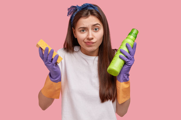 清洁剂管家和清洁概念年轻的女看门人留着长发 拿着海绵和装有清洁剂的绿色瓶子 戴着保护手的橡胶手套 做家务工人看门人不满
