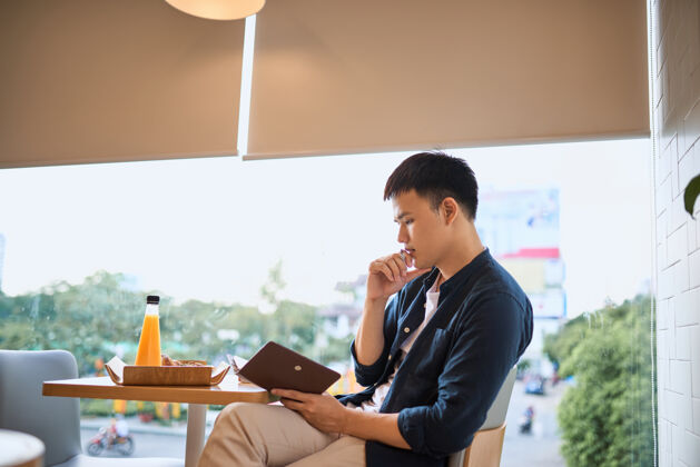 好商人在咖啡馆窗口的笔记本上写字 专注于工作 自信的年轻人一边坐在咖啡馆里写字一边在笔记本上工作 年龄20-30岁男士阅读早晨