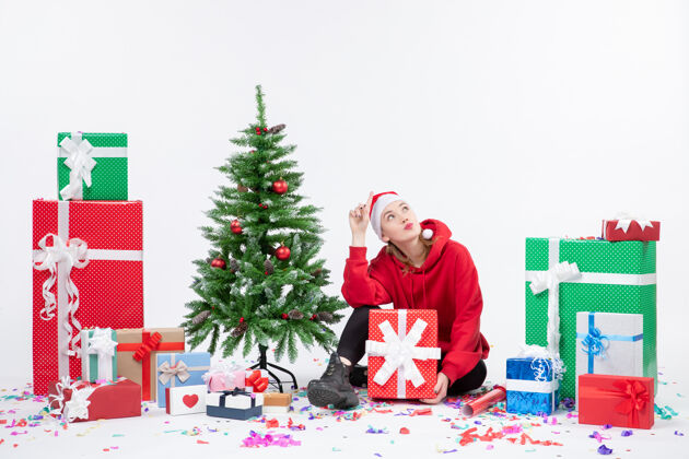 冬天年轻女子坐在白色墙壁上围着节日礼物的正视图圣诞快乐庆祝礼物