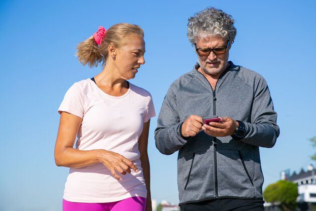 电话关注男性慢跑者在慢跑后使用手机上的健身应用程序成年夫妇穿着运动服 站在外面交流和运动概念的小工具活动跑步中等拍摄
