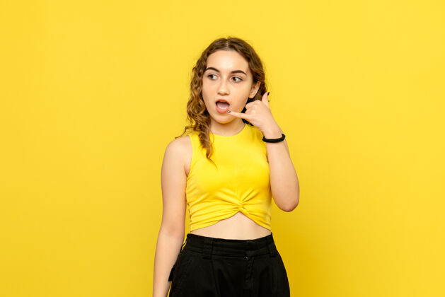漂亮黄色墙上年轻女子模仿电话的正面图模仿人时尚